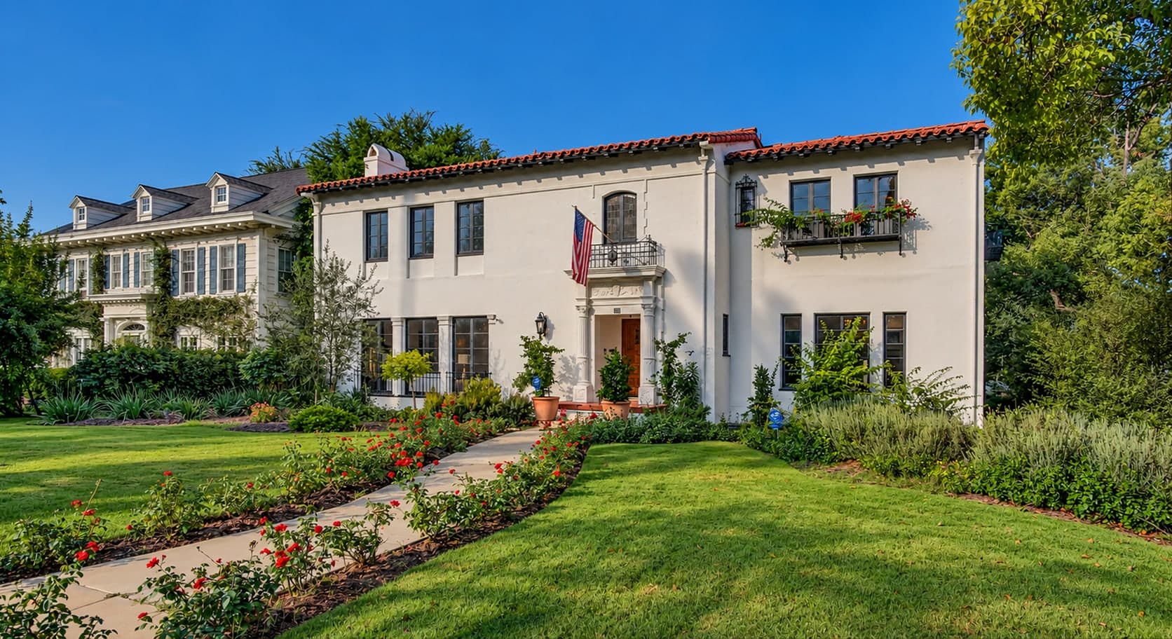 White Spanish-style home with a tiled roof, roses along the front walk